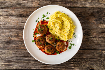 Fried pork meatballs with potato puree and tomato sauce on wooden table
