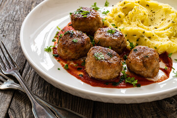 Fried pork meatballs with potato puree and tomato sauce on wooden table
