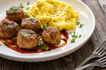 Fried pork meatballs with potato puree and tomato sauce on wooden table
