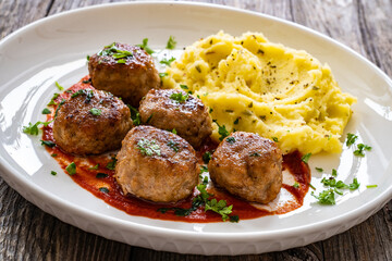 Fried pork meatballs with potato puree and tomato sauce on wooden table
