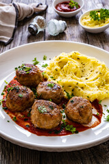 Fried pork meatballs with potato puree and tomato sauce on wooden table
