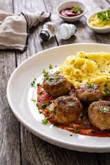 Fried pork meatballs with potato puree and tomato sauce on wooden table
