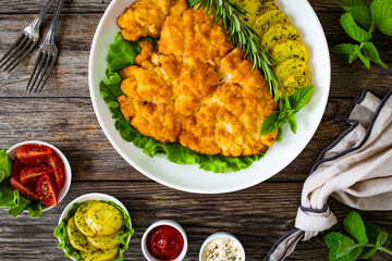 Breaded fried pork chop with fried potatoes and greens on wooden table
