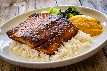Fried teriyaki salmon steak with white rice, mango, cucumber and wakame on wooden table
