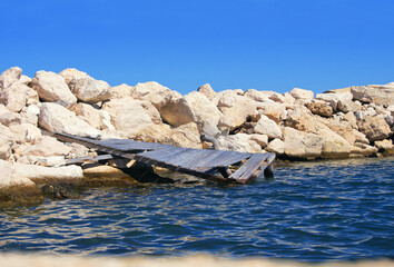 Kaputter Holzsteg an einem Wellenbrecher aus Steinen, horizontal 