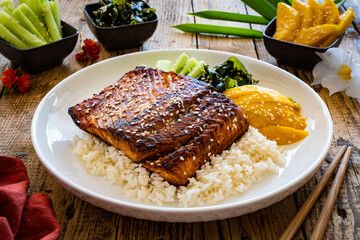 Fried teriyaki salmon steak with white rice, mango, cucumber and wakame on wooden table
