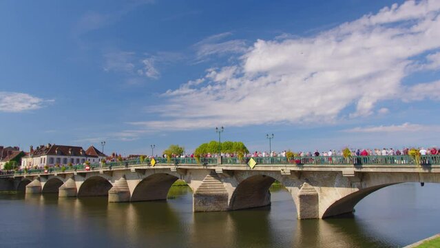 A large crowd of people on the bridge. Traffic from people. Time lapse. Beautiful clouds in the background of the old bridge. View of city landscape of Joigny on River Yonne, Burgundy, France