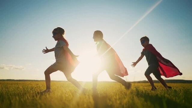 team superhero. a group of children are running across the field in a superhero costume with a silhouette of a red cape at sunset. the concept of a happy family childhood dream. teamwork superhero