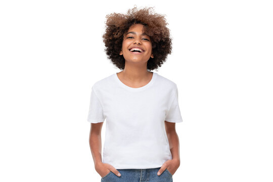 Front view of laughing african teen girl standing with hands in pockets, wearing white tshirt with copy space