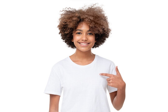African student girl pointing with index finger at blank white t-shirt with empty space for your advertising text or image, standing isolated