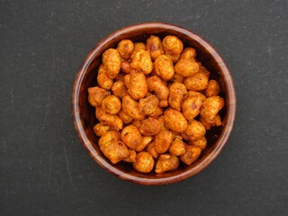 Masala peanuts in a wooden bowl on black background 