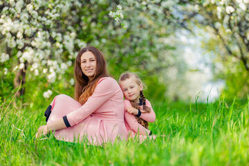 Fototapeta premium mother and daughter sit in a flowering garden with their backs to each other