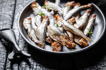 Healthy smoked sprats on a black plate and burnt table.