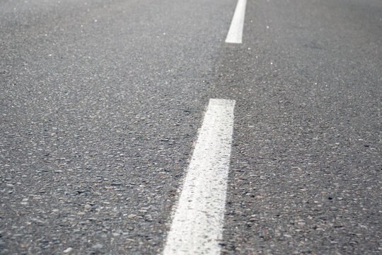 White line markings on the road. The dividing strip of the road markings on the asphalt close-up. View of the asphalt from the marked, side view.