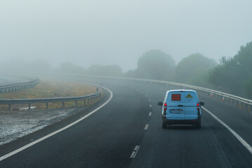 Van with radioactivity hazard plates, class 7 of the ADR code, driving on a highway on a foggy day.