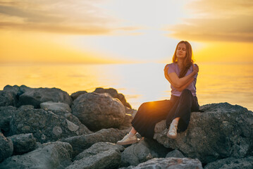 portrait of a woman hugging herself at sunset in summer by the sea - obrazy, fototapety, plakaty