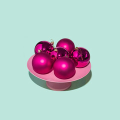 Xmas baubles and pastel pink cake plate stand on light mint background. Minimalistic Christmas decoration concept. Modern New Year composition. Winter holiday idea.