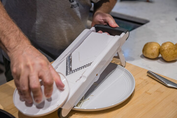 Mandolin slicing raw potato in home kitchen.