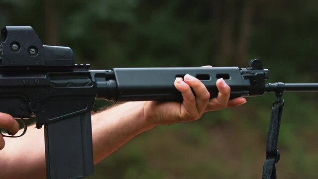 Elegant black brand-new rifle with professional collimator being held and used by unrecognizable caucasian person. Outdoor shot. Shell-case flying out. High quality 4k footage