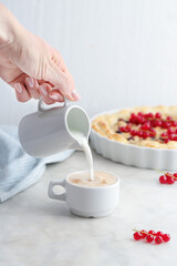 Young woman pouring milk from jug into coffee cup