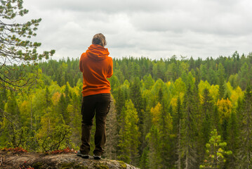 a woman in a hoodie and trousers stands on the edge of a cliff against the background of a forest. the concept of travel and tourism