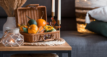 Cozy autumn concept. Home warmth in cold weather. Still-life. Pumpkins, wicker basket, candles and flowers on the coffee table in the home interior of the living room.