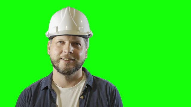 a male engineer worker in a construction helmet smiles portrait on a green background
