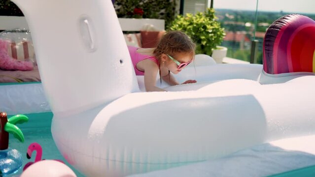 cute baby girl having fun in anflatable pool at the patio at home on summer day