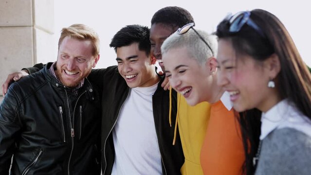 Diverse group of united young friends laughing together outdoor - Multiracial teenager students having fun hugging each other in street - Team, community and unity concept