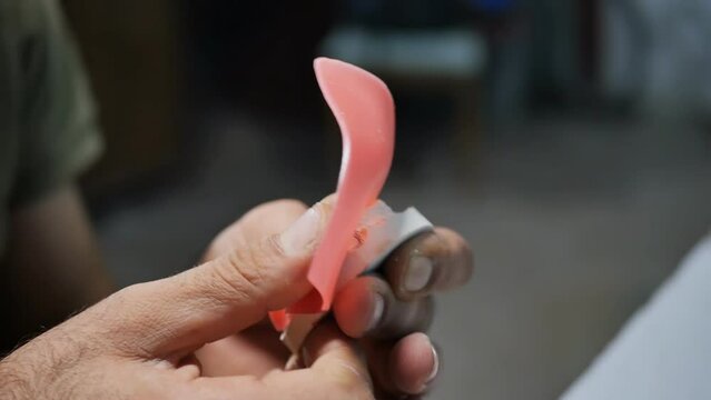 the process of making a denture in the workshop of a dental technician. The hands of a dental technician create artificial gums from red soft paraffin on a cast of the patient's jaw