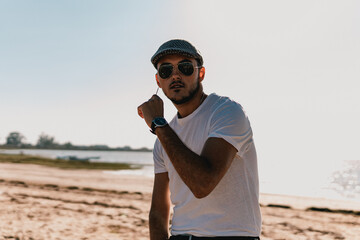 Hombre joven modelo con camisa, gorro y gafas de sol en una playa