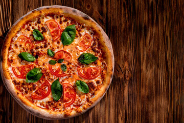 Delicious fragrant pizza with mozzarella, tomatoes and basil with tomato sauce on woden background. Top view