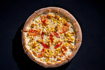 Pizza for children on a cream base with chicken fillet, tomatoes, corn and mozzarella cheese on black background