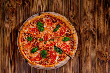 Delicious fragrant pizza-Margherita with mozzarella, tomatoes and basil on tomato sauce on woden background. Copy space