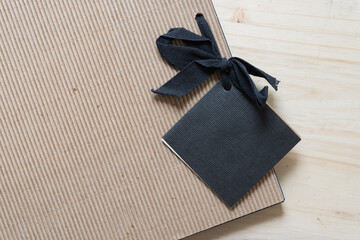 photo album with plain brown corrugated paper covers, black gift tag, and black ribbon on wood