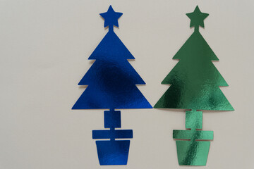 two metallic blue and green holiday trees standing side by side on blank paper