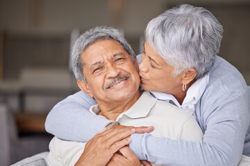 Happy Mexico senior couple kiss on living room sofa for love, care and trust in romantic relationship at house or home. Elderly people or retirement man and woman smile, hug and kissing face cheek