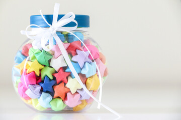 Close up of glass jar of colourful origami paper lucky stars tied with a white ribbon. Handcrafted gift meaning love and luck.
