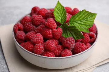 Bowl of fresh ripe raspberries with green leaves on table, closeup