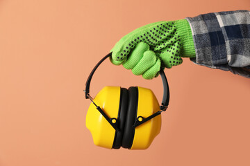 Worker holding safety headphones on coral background, closeup. Hearing protection device