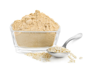 Sesame flour in glass bowl and spoon of seeds isolated on white