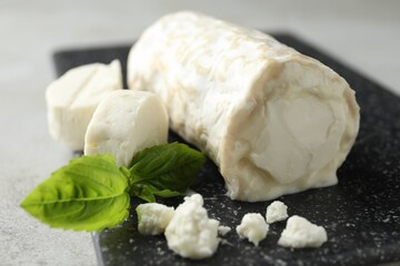 Delicious fresh goat cheese with basil on black board, closeup