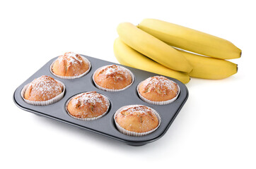 Ripe bananas and tasty homemade muffins powdered with sugar in tray on white background