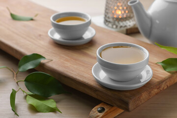 Tray with white cups of green tea, leaves and teapot on wooden table, closeup