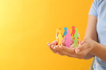 Woman holding paper human figures on yellow background, closeup with space for text. Diversity and inclusion concept