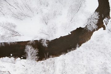 Beautiful aerial view of snow covered pine forests and a river winding among trees. Rime ice and hoar frost covering trees.