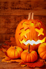 Spooky jack o`lantern and dry autumn leaves on wooden table. Halloween decor
