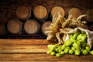 Fresh hops and wheat spikes on wooden table in beer cellar, space for text