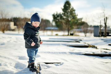 Fototapeta na wymiar Funny toddler boy having fun outdoors on chilly winter day. Child exploring nature.