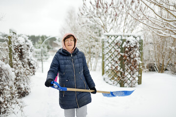 Senior woman shoveling snow off a walkway after massive snowfall.